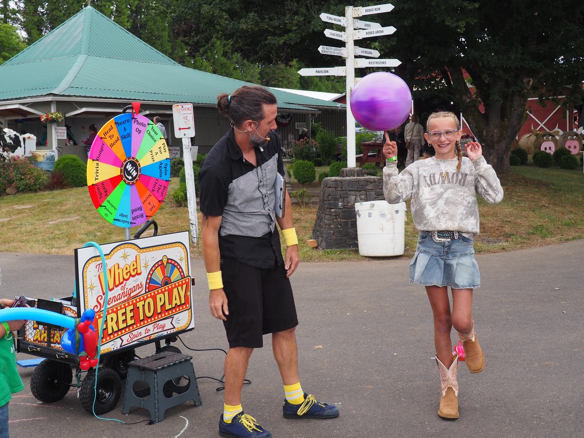 Matt Baker beside the Wheel of Shenanigans cart at a county fair while a girl spins a ball on her finger