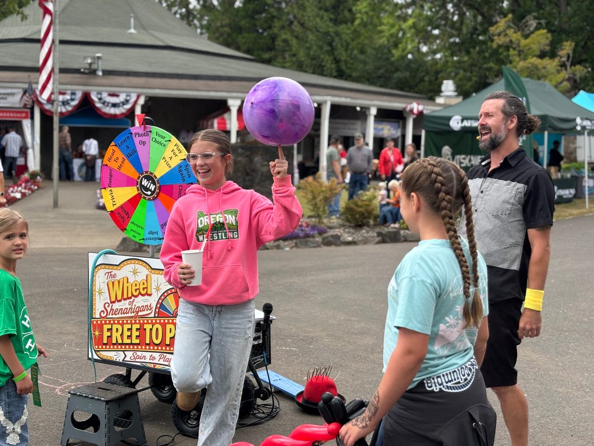 A girl laughing as she balances a spinning ball on one finger, with a crowd of kids watching